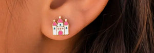 A close-up of a person's ear wearing a small castle stud earring. The earring features a white body with pink roofs and gold-toned outlines and accents.